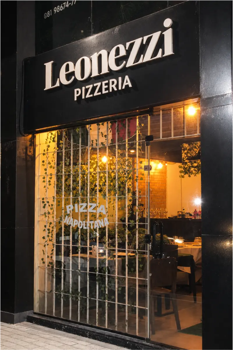 Fachada da Leonezzi Pizzeria à noite, com o salão iluminado visto da rua